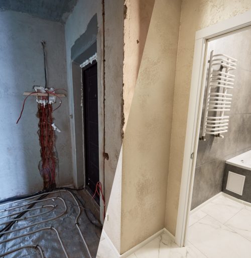 Horizontal image, view from the corridor to finished bathroom and to unfinished other room with heating pipe system on the floor. Concept of home renovation and refurbishment.